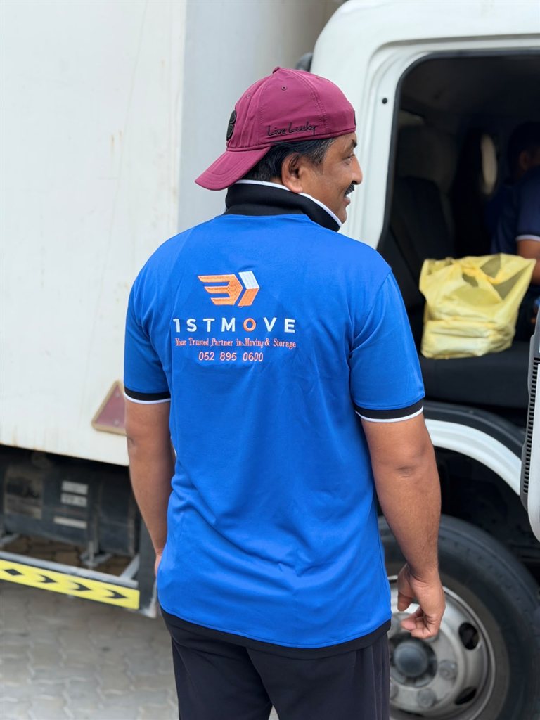 أحد أفراد طاقم 1stMove الحقيقي بزي رسمي يقف بجانب شاحنة نقل تابعة لـ 1stMove في دبي