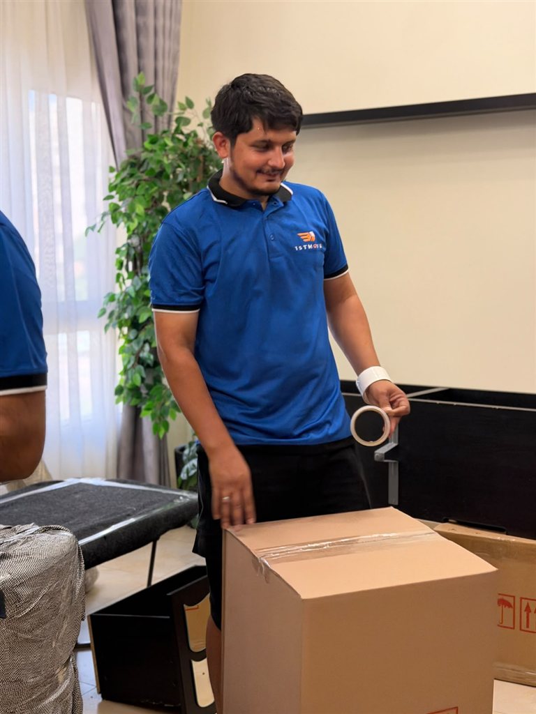 أحد أفراد طاقم 1stMove الحقيقي يقوم بتحميل أثاث مغلَّف في شاحنة نقل تحمل علامة الشركة